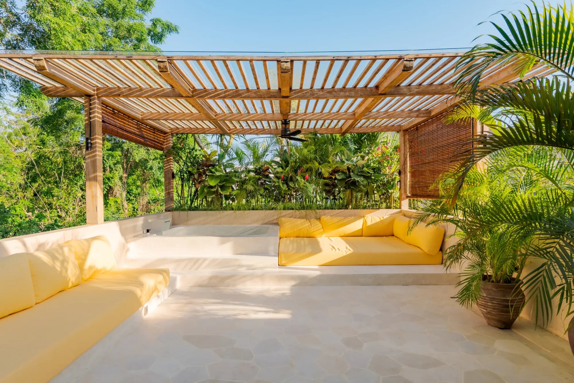 Outdoor lounge area under wooden pergola with tropical plants